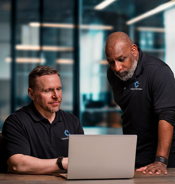 Two Digital Bodyguards team members in branded black polo shirts standing outside an ivy-covered stone building